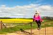 © Leah-Anne Thompson - Female sits on rusty old gate overlooking canola fields