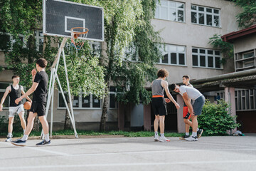 Friends enjoy playing basketball together on an aged court in their neighborhood, showcasing teamwork and outdoor fun on a sunny day.