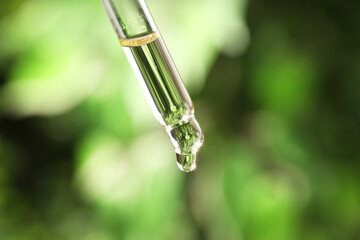 Wall Mural - Essential oil dripping from pipette against blurred green background, closeup