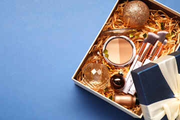 Makeup brushes, decorative cosmetics, perfume and Christmas decor in box on blue background, top view. Space for text