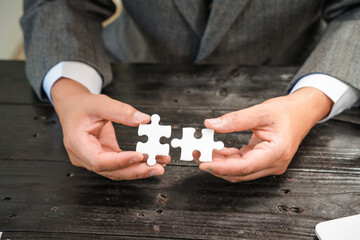 A group of people are putting together a jigsaw puzzle and trying to put the pieces together. This is a scene where everyone is working together on a wooden table, holding a jigsaw puzzle.