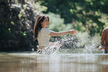 A joyful young woman enjoys a refreshing day outdoors, playfully splashing water in a tranquil natural environment. The image captures happiness, freedom, and the beauty of nature.