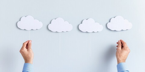 A pair of hands holds four cut-out cloud shapes against a light background, symbolizing creativity, ideas, or a dreamy concept.