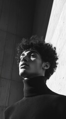 Poster - A man with curly hair is wearing a black sweater and looking up at the camera