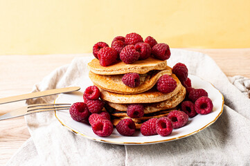 Delicious whole wheat healthy pancakes with raspberry, fork and knife styling natural light and copy space on the table with linen cloth background lifestyle