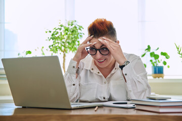 Portrait of surprised mature woman working at home on computer laptop