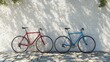 © Olga - Two bikes parked beside each other in front of a white brick wall with a tree shadow