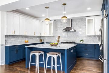 Wall Mural - A luxurious white and blue kitchen with gold hardware, stainless steel appliances, and white marbled granite countertops. No brands or labels.