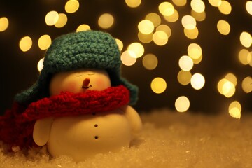 Wall Mural - Cute decorative snowman on artificial snow against blurred lights, closeup. Space for text