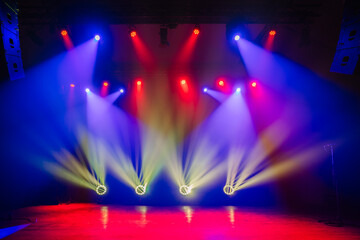 Colorful stage lights shine in vibrant blue, red, and yellow hues, illuminating the empty stage and creating an energetic atmosphere for performances..