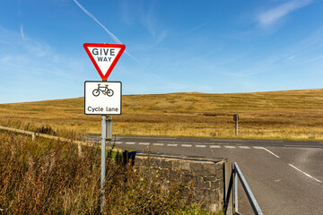 Give Way and Cycle Lane road signs at road junction on rural countryside road with blue sky horizon