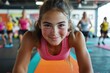 © Milos - A young woman in a pink tank top smiling as she leads a fitness class, engaging in a plank position with a group of people working out in the background.