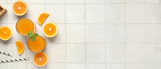 Wall Mural - Glasses of fresh orange juice with mint and cut fruits on white tile background