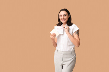 Wall Mural - Beautiful young woman holding pad and calendar with marked days of menstruation on brown background