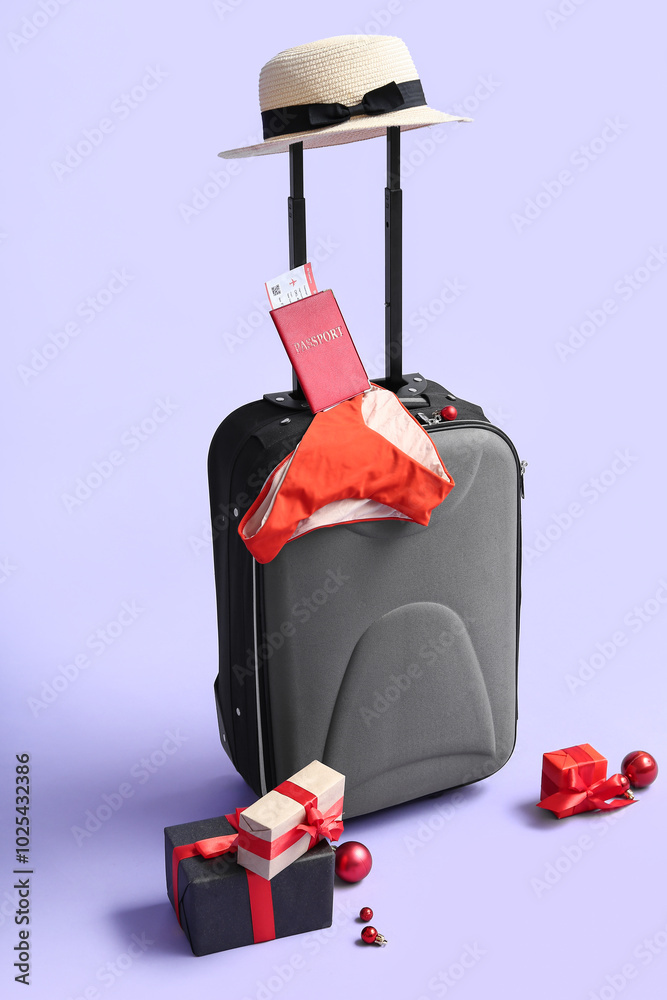 Suitcase with beach accessories, passport and Christmas gift on color background
