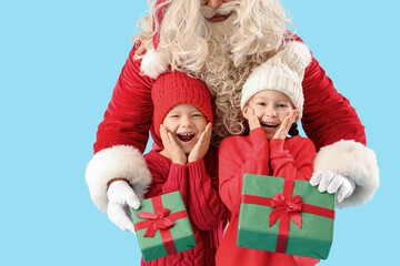 Surprised little children receiving Christmas gifts from Santa Claus on blue background