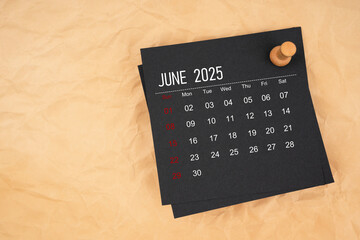 Black calendar sheet for June 2025 with thumbtack on brown paper crumpled.