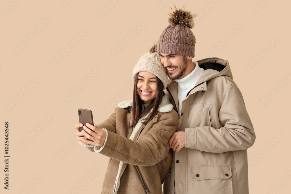 Loving couple in winter clothes taking selfie on beige background