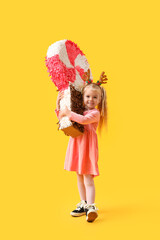 Wall Mural - Cute little girl in reindeer horns with candy pinata on yellow background