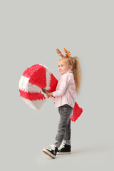 Wall Mural - Cute little girl in reindeer horns with candy cane pinata on light background