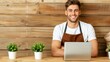 © ChimE - Joyful young florist in an apron working at a desk in a floral shop, managing tasks on his laptop with a smile.