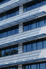 A close-up view of a modern building facade featuring a geometric pattern of blue and white panels with rectangular windows. 