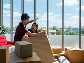 Asian cheerful couple family laughing and packing boxes together in a sunlit apartment, surrounded by moving supplies, with a city view through windows in the background