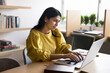 © fizkes - Positive young Indian professional girl typing on laptop in co-working room working at computer, smiling, browsing Internet, using online application for business communication