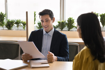 Sticker - Positive young Hispanic businessman interviewing job candidate woman, reading paper resume at meeting. Financial advisor, legal expert and customer meeting for consultation, discussing document