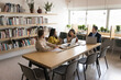 © fizkes - Multiethnic small team of business colleagues talking in academic co-working space, discussing teamwork at large table. Group of adult students meeting in library, brainstorming on training project