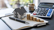 © Rsquare stock - tax day background,House model, house placed on a white surface, next to a calculator, a pencil, and some coins, symbolizing home finances, budgeting, or real estate planning.
