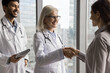 © fizkes - Two diverse physicians in charge congratulate young lady with successful recovery shake patient hand discharging from hospital. Doctors team handshaking with medical insurer appreciate for partnership