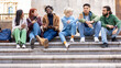 © Lomb - Diverse students relaxing on campus stairs, multicultural friends using smartphones and socializing outdoors