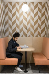 Canvas Print - Focused young Arab employee using digital gadget in office booth, freelance cafe cubicle. Entrepreneur, businessman, freelancer man sitting in separate rental workplace, typing on smartphone