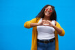 © Sanc/peopleimages.com - Portrait, woman and sunglasses with heart sign in studio for love icon, advertising romance and date opinion. Smile, girl and hand gesture with review, support and passion feedback on blue background