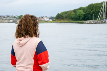 A young brunette woman stands with her back to the camera, gazing at a serene seascape with a peaceful island with lush green vegetation