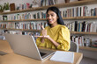 © fizkes - Sign language therapist talking on video call. Happy young Indian teacher woman speaking to student with hearing disability, showing hand gesture at laptop, working at computer in library