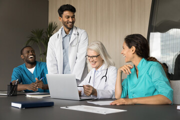 Young team medics interns medical faculty students gather on seminar training holding by mature female doctor professor. Multicultural teammates listen to leader analyzing clinical case using laptop