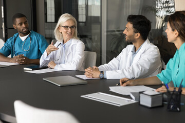 Experienced senior female professor of medicine clinical specialist lead multiethnic doctors group training workshop practicum at modern clinic. Friendly medic team listen to mature leader on seminar