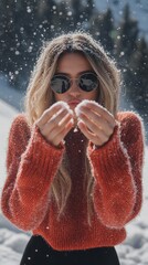 A woman in a red sweater is blowing snow out of her mouth