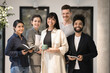 © fizkes - Small company diverse staff corporate head shot portrait. Happy multiethnic business team posing in office interior, standing together, holding tablet, notebook, smiling, looking at camera