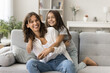 © fizkes - Sweet family moments. Happy laughing young mama little junior schoolgirl daughter play funny active game on large couch having fun together. Friendly elder younger sisters cuddle tickle giggle on sofa