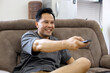 © Gatot - Smiling Asian Man Watching Movie on TV While Enjoying Sitting on Sofa