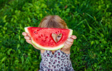 Poster - A piece of watermelon in the hands of a child in a park. Selective focus.