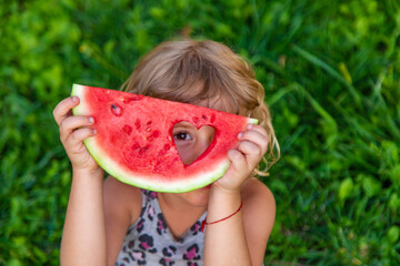 Wall Mural - A piece of watermelon in the hands of a child in a park. Selective focus.