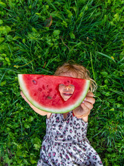 Wall Mural - A piece of watermelon in the hands of a child in a park. Selective focus.