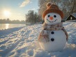 © Iurii - A cheerful snowman stands by a frozen lake at sunset with a cozy winter hat and scarf