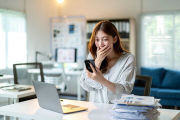 A woman is sitting at a desk with a laptop and a cell phone