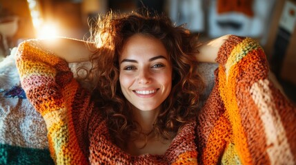 A cheerful woman with curly hair wearing a colorful, knitted sweater, expressing warmth and comfort in a relaxed setting with sunlight softening the scene.