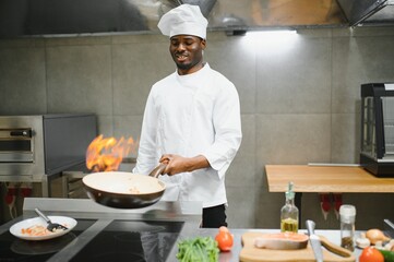 African american chef prepare food with fire at kitchen restaurant. Chef with wok at kitchen